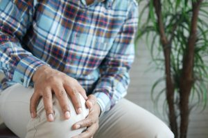 Close-up of a man's hands firmly clutching his knee in pain, highlighting the area of a meniscus injury against a neutral background.